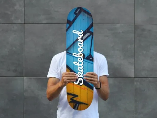 Front Sight of Man Holding Skateboard Mockup Against Wall 1
