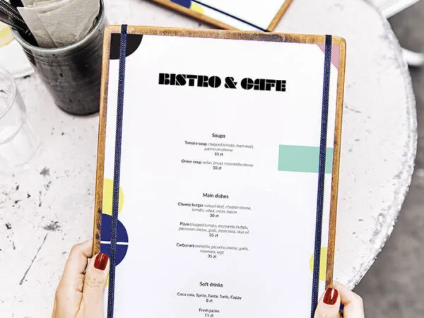 Mockup Featuring Hand Holding Restaurant Menu with a Table at Background 1