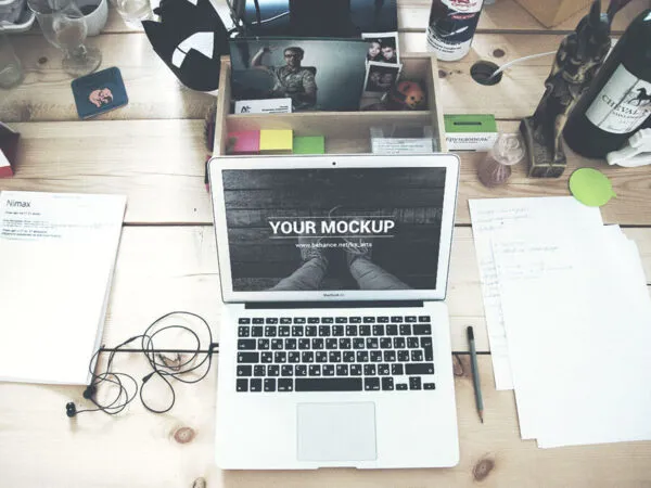 Opened MacBook on a Busy Wooden Table Mockup 1