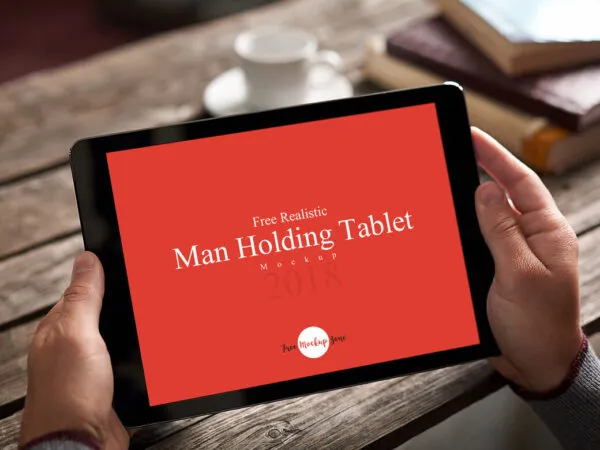Realistic Man Holding Tablet on Wooden Table Mockup 1