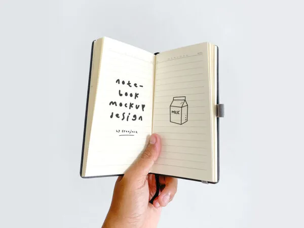 Top View Hand Holing Small Notebook Mockup in Plain Setting 1